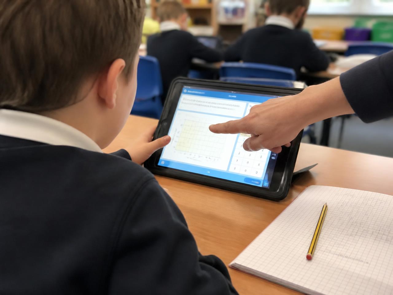Alumno usando una tablet en su mesa de clase junto a su cuaderno